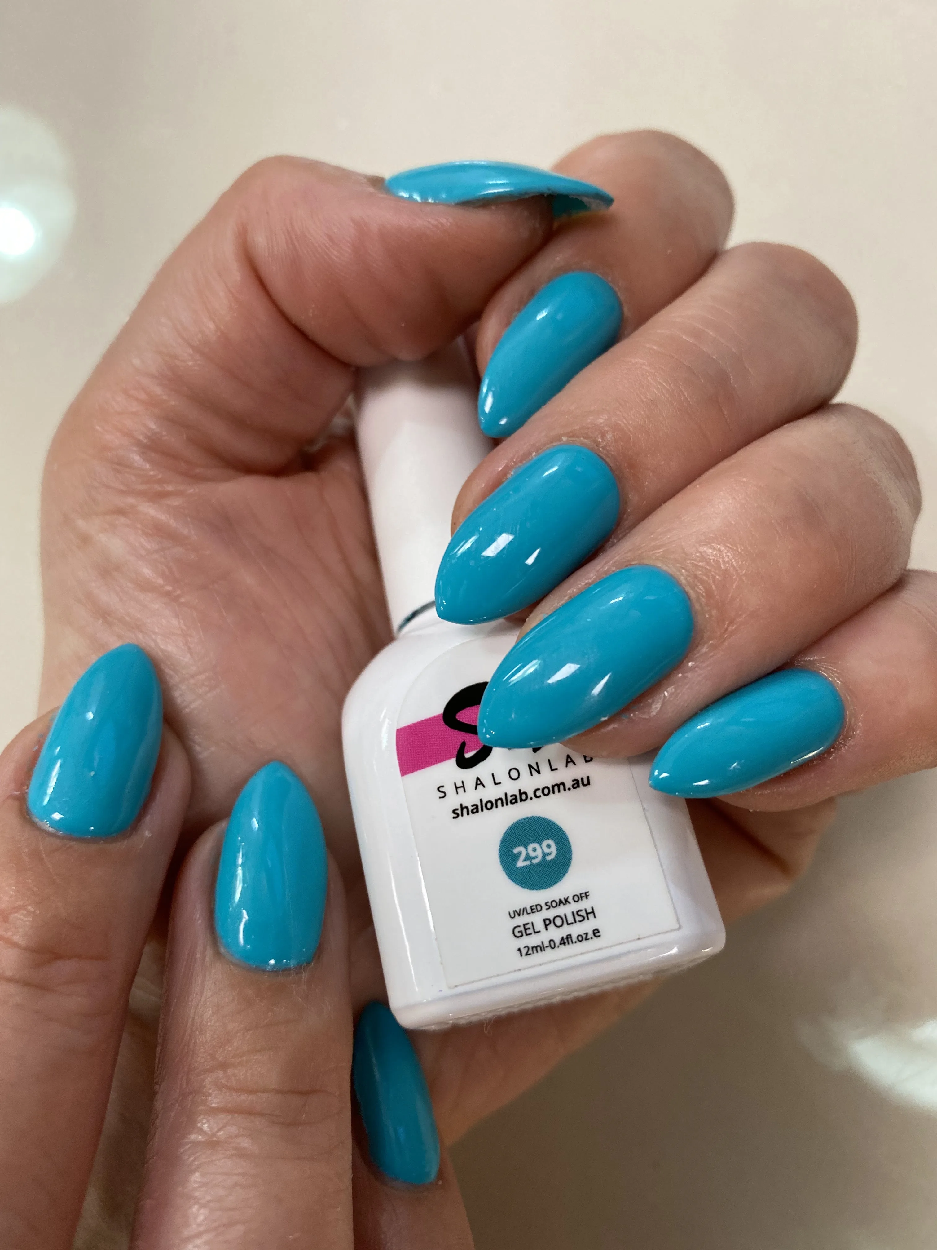 Teal and blue almond nails beside a Shalonlab gel-polish bottle