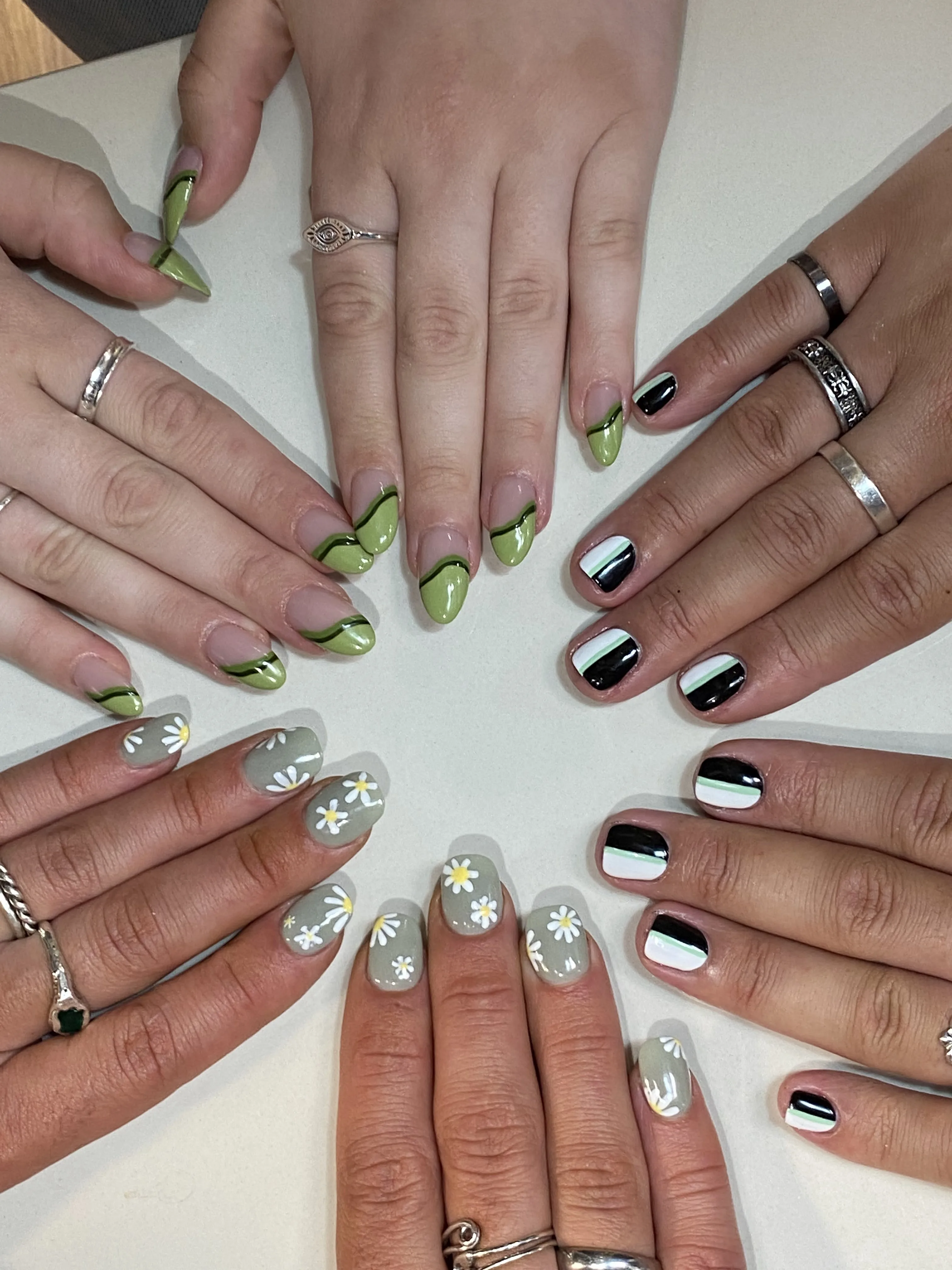 Four hands showing varied nail art — sage swirls, stripes, and daisies