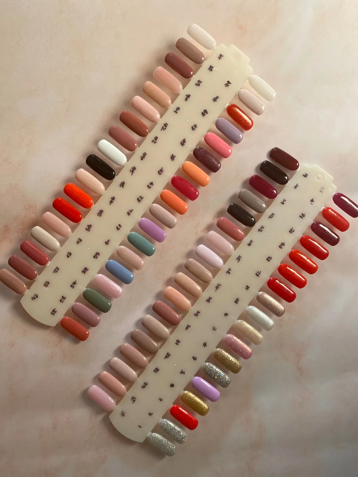 Two nail colour-sample display sticks fanned with dozens of gel swatches on marble — the Organique colour range